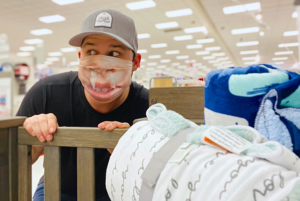 man standing in front of baby crib wearing runny nose face mask