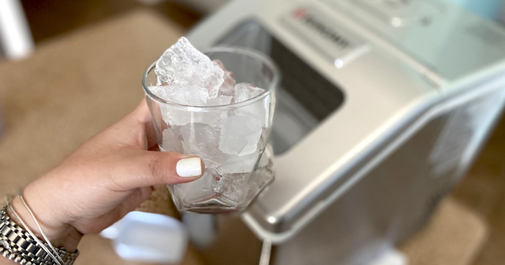 holding cup filled with ice with ice maker in the background 