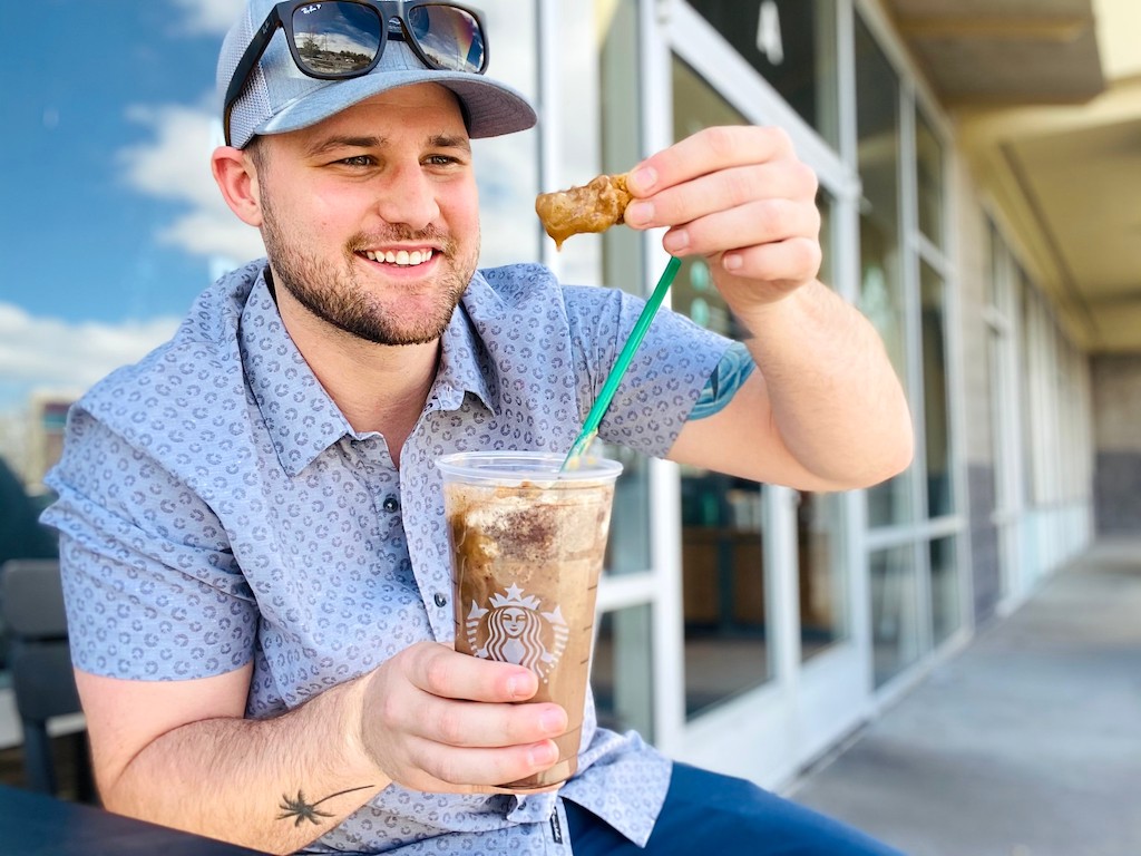 man holding Starbucks frapp in one hand and chicken in the other