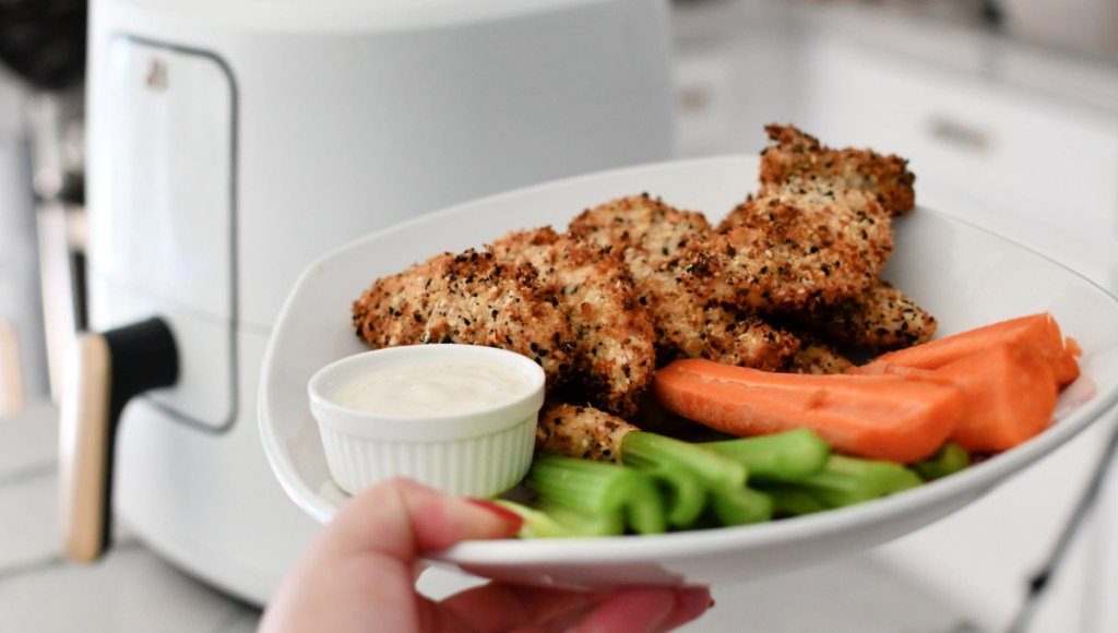 holding plate of chicken tenders near air fryer