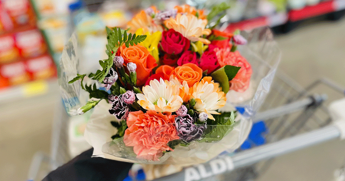 woman holding orange bouquet of flowers near aldi shopping cart