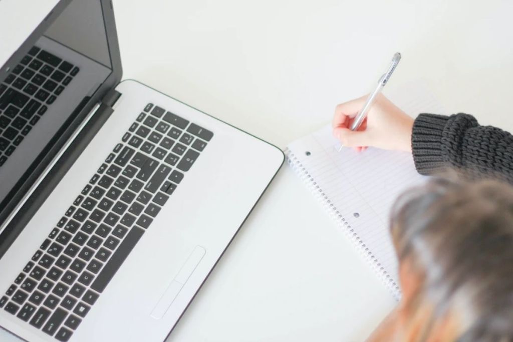 Person using laptop and pen and paper