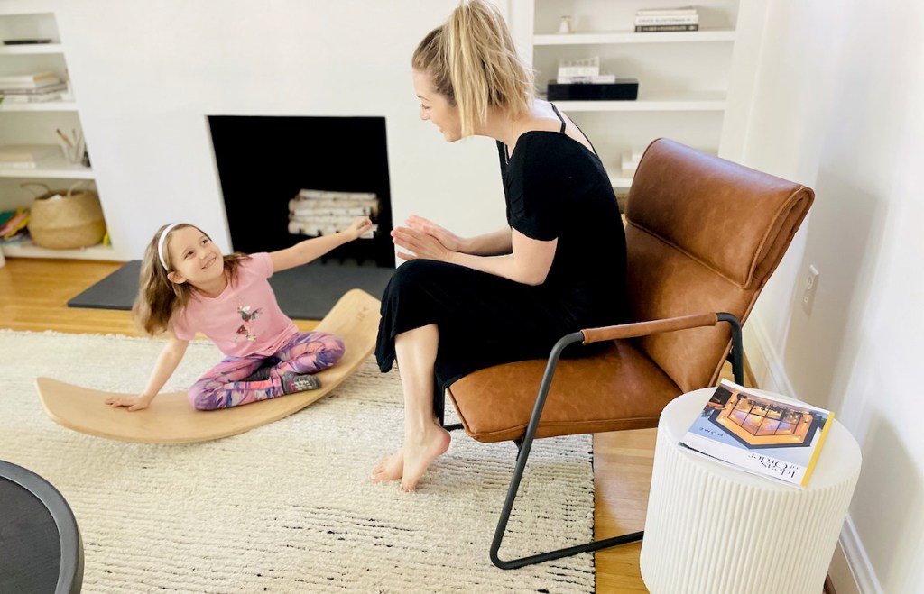 girl playing on balance board next to woman on leather sling chair