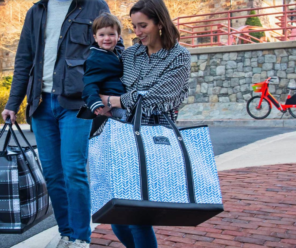 woman holding little boy and large tote bag walking on brick sidewalk