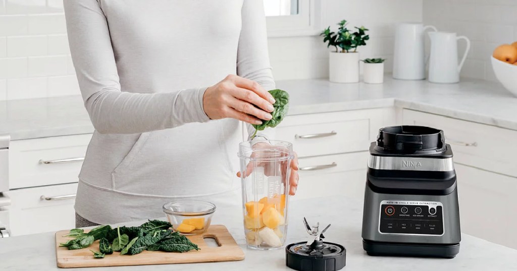 woman adding spinach to a blender cup