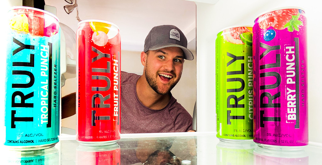 smiling man looking into his fridge and seeing cans of hard cider