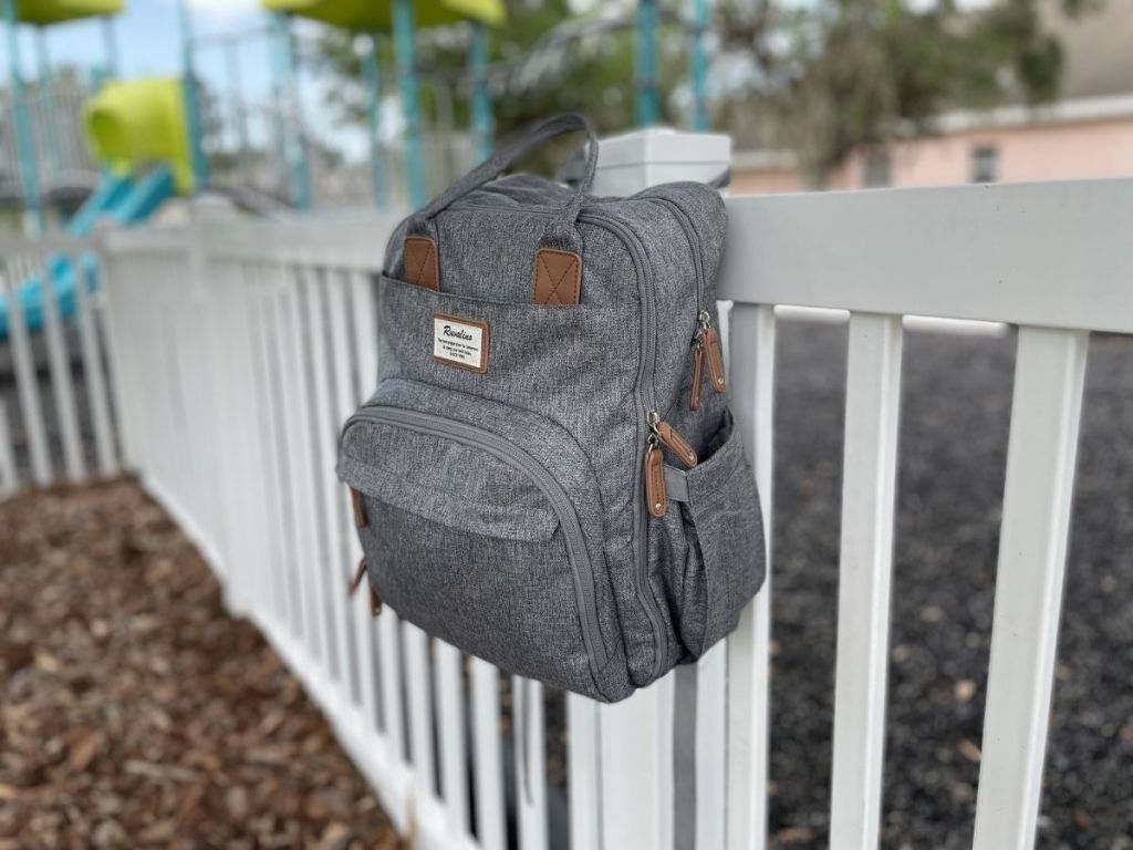 gray backpack diaper bag hanging on white fence