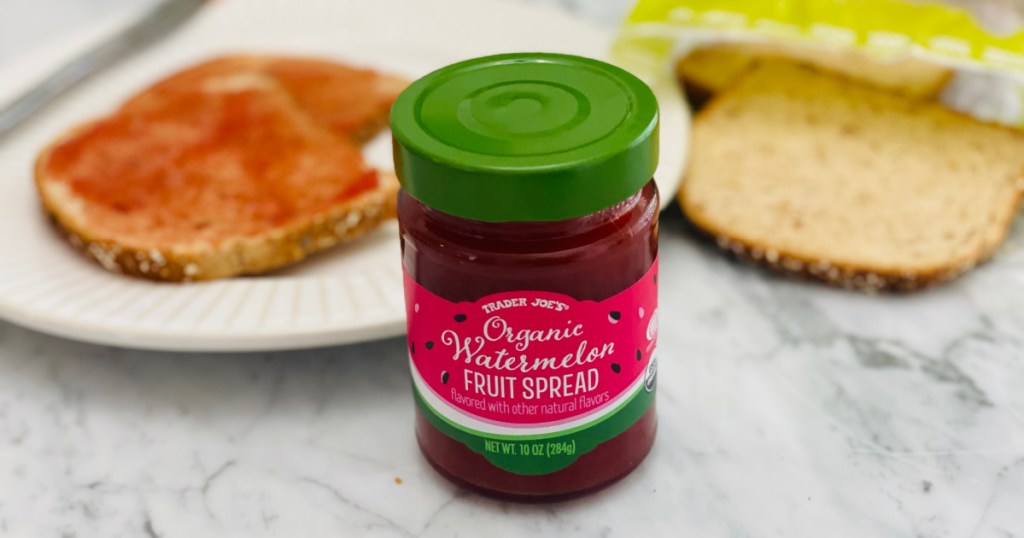 jar of fruit spread on table near bread and plate