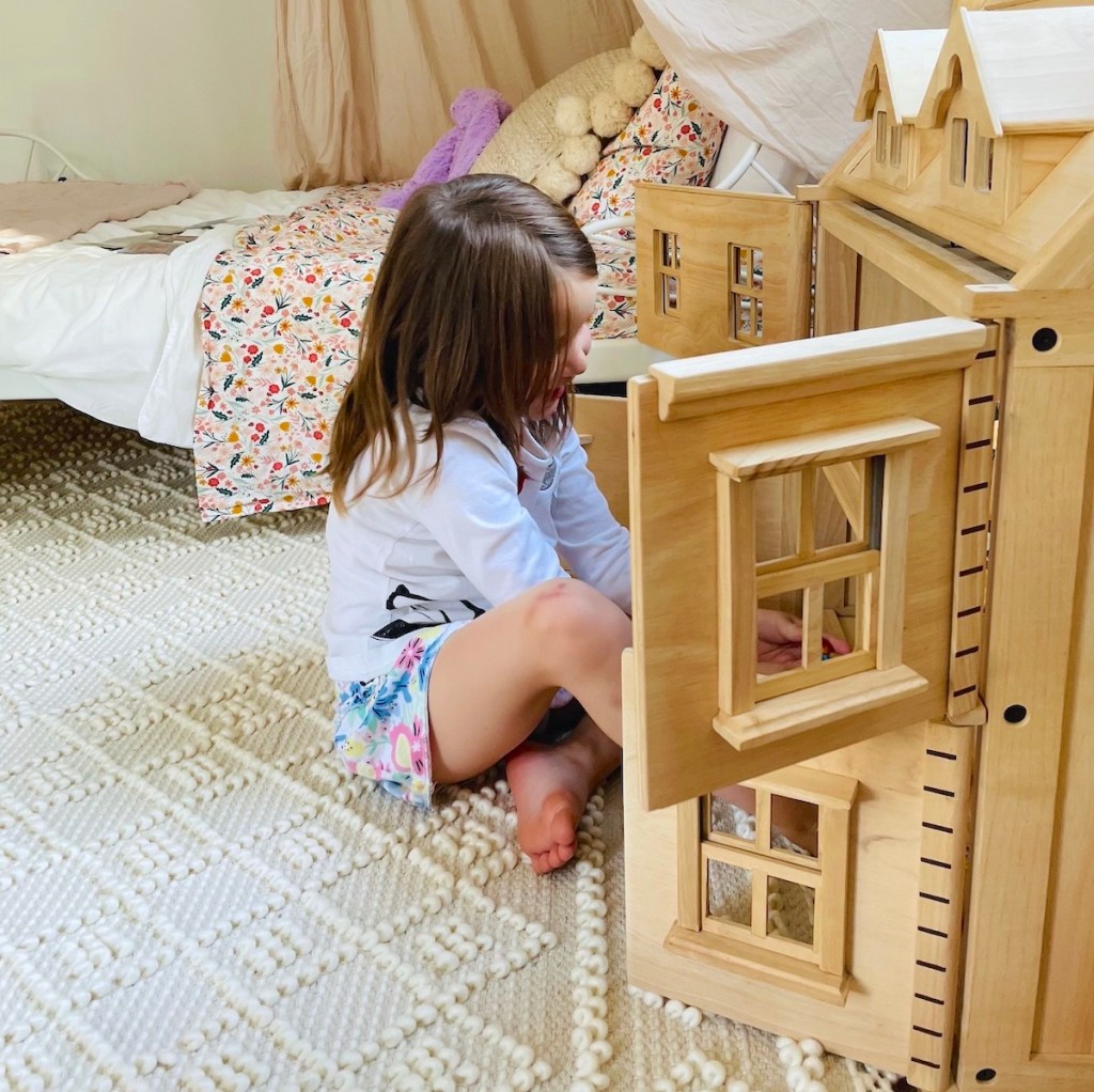 girl playing on rug with wooden dollhouse