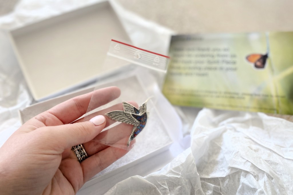 hand holding cremation jewelry hummingbird with box in background