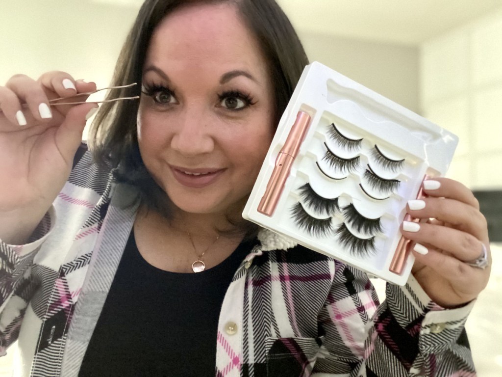 woman holding up box of false lashes while holding tweezers up to eyeball