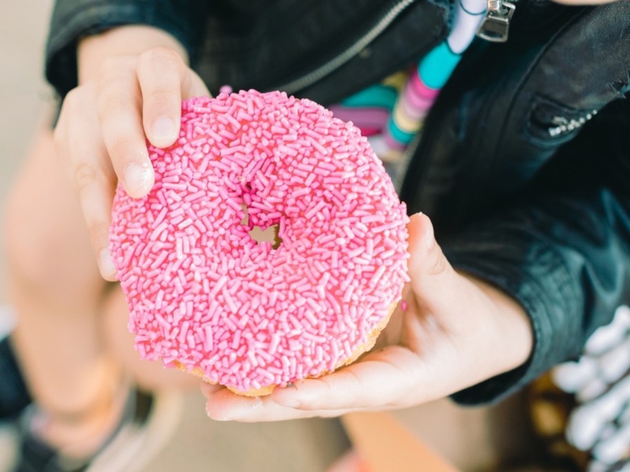 holding a pink donut with sprinkles what to buy in june 