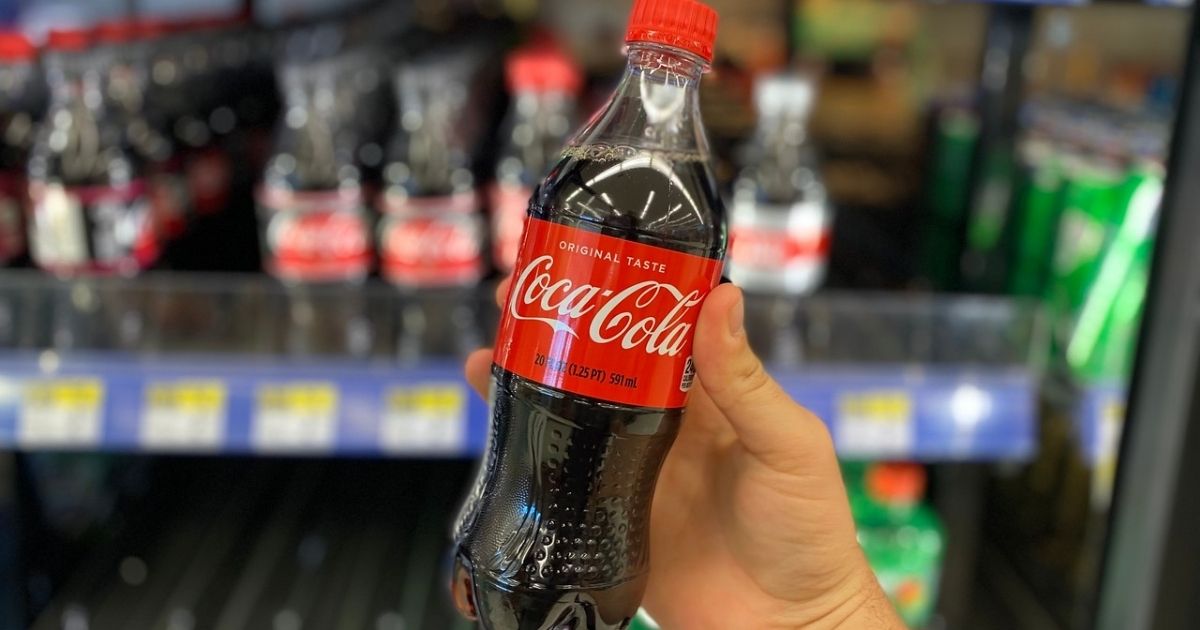 hand holding up a 20oz bottle of coca-cola in front of a walgreens refrigerator case