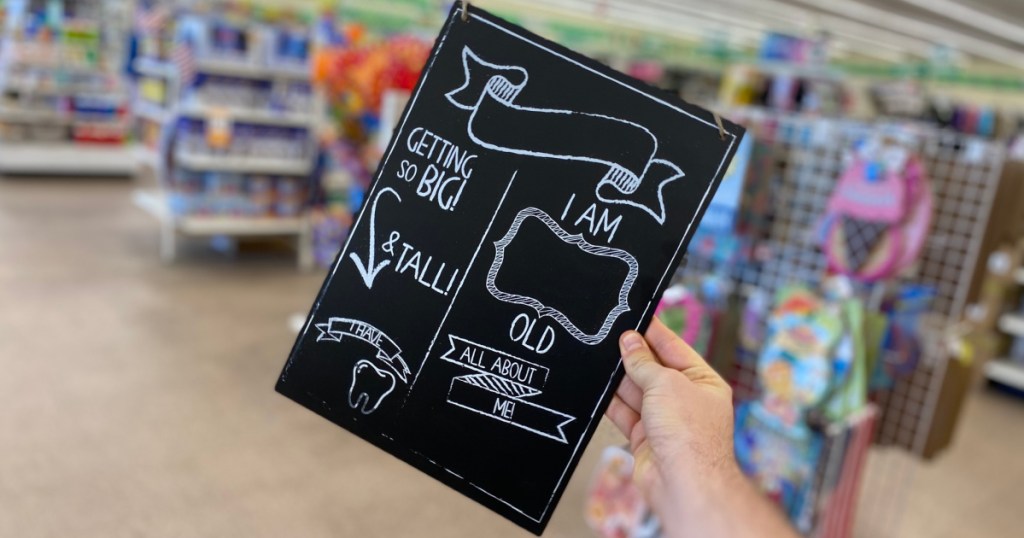 hand holding baby milestone chalk board near in-store display