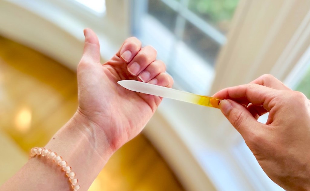 hand holding file against nails in front of window