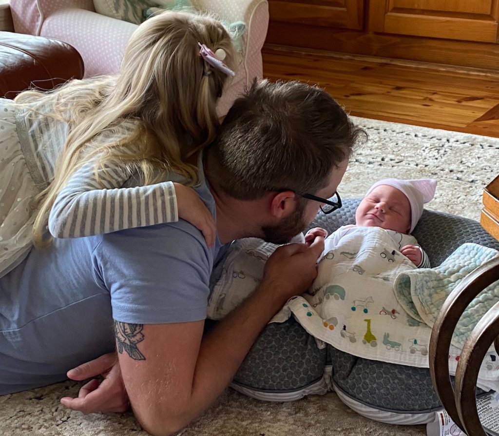 man laying on floor with toddler and newborn baby