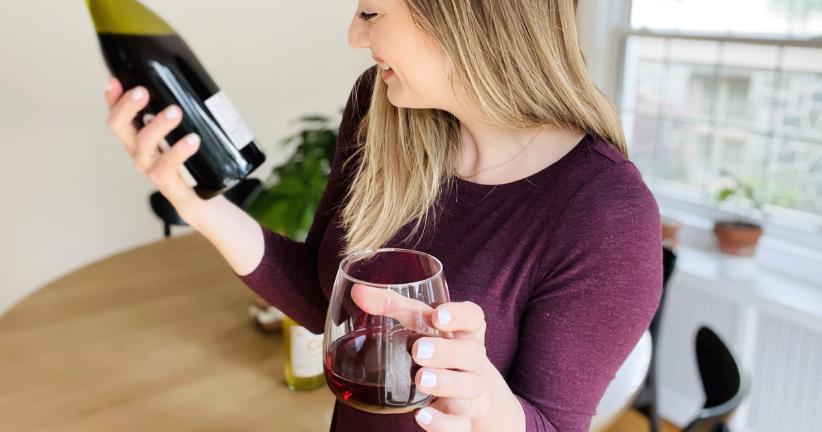 woman holding bottle of red wine and holding wine glass