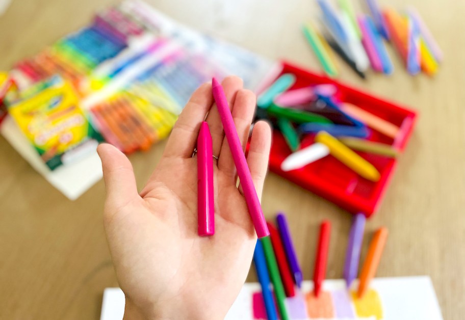 hand holding two pink crayons over table of crayons