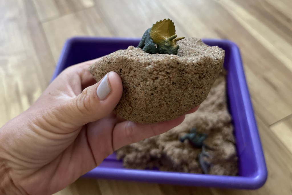 hand holding dinosaur in kinetic sand