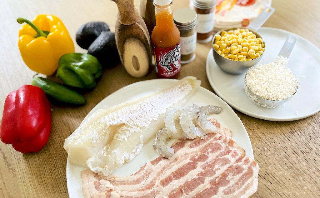 raw fish shrimp and bacon on plate with other fresh ingredients and spices on table