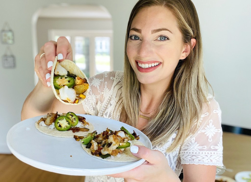 woman holding up fish taco on white plate