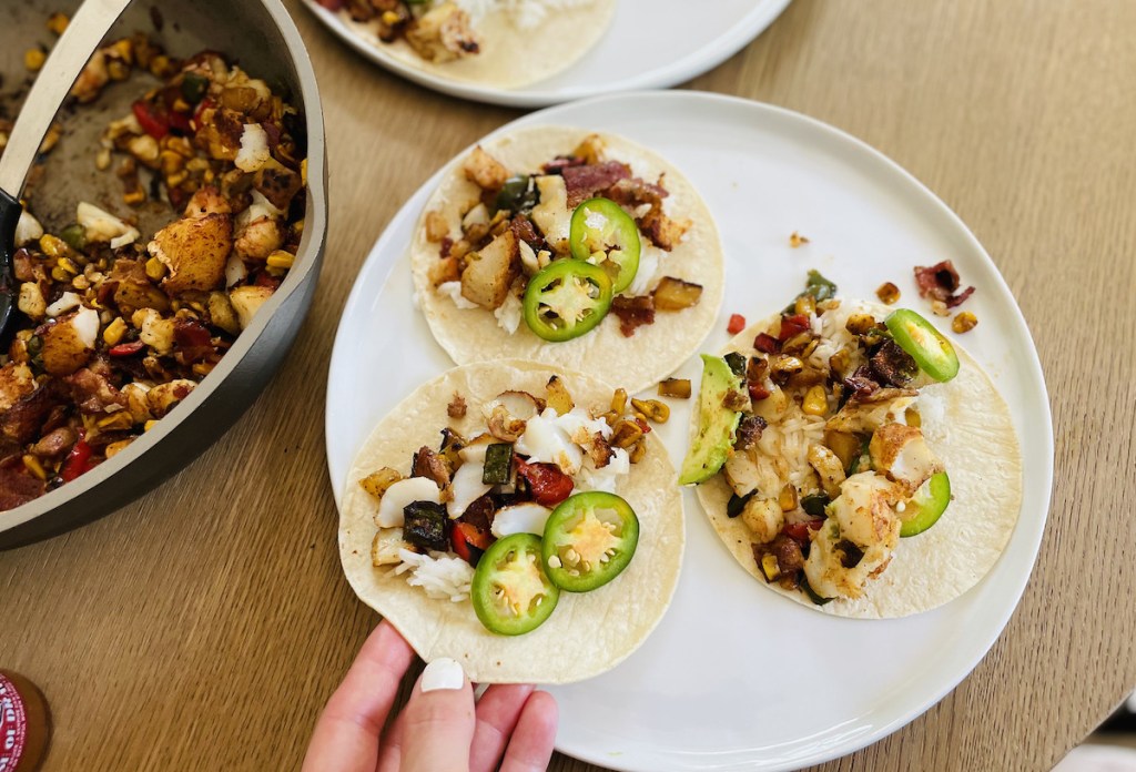 hand holding a fish taco on plate