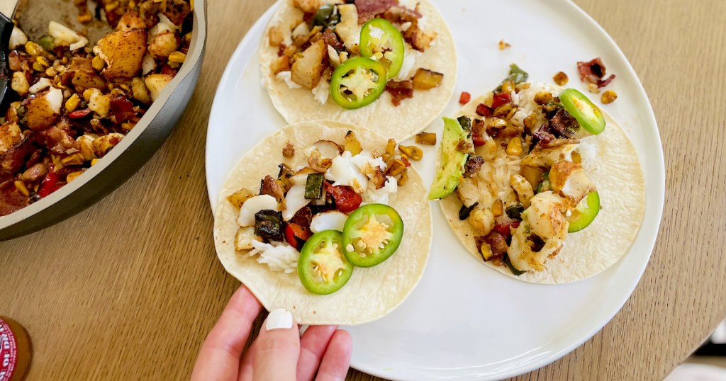 hand holding fish taco on plate