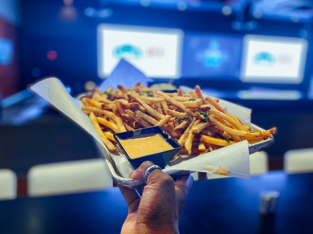 hand holding a plate of french fries in front of sports bar