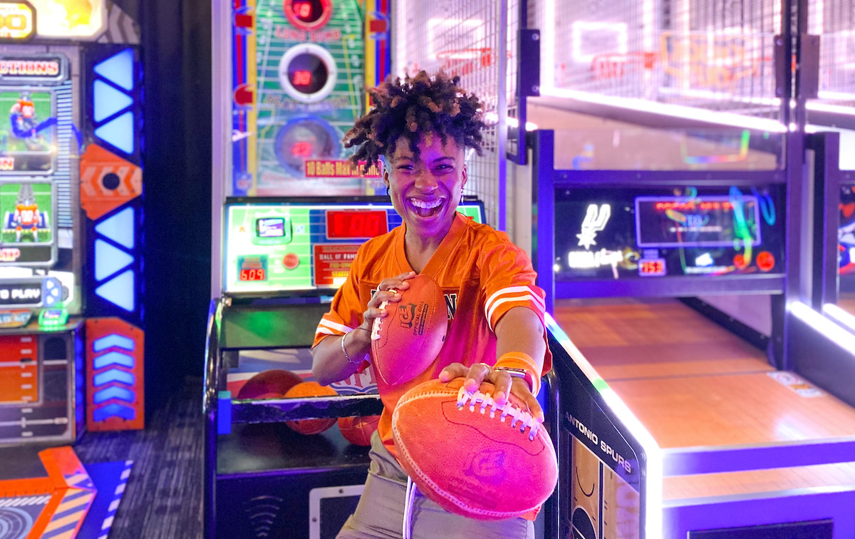 woman holding two footballs in gaming room 