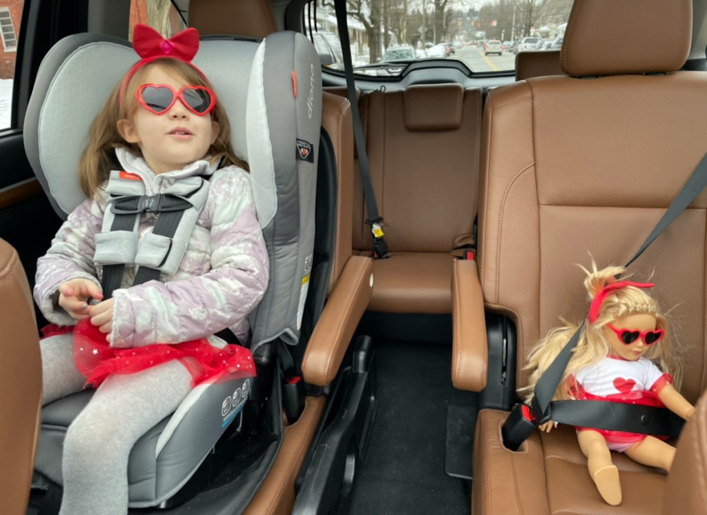 girl sitting in car seat with doll in passenger seat