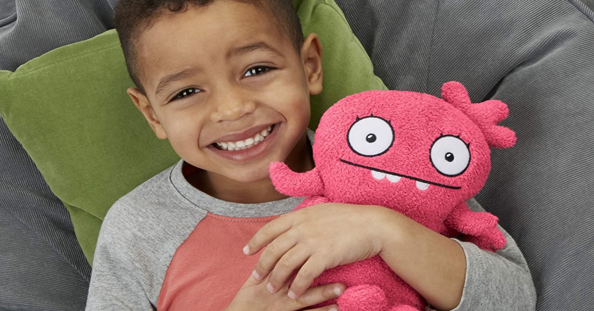 boy in a soft chair with a green pillow holding a pink plush uglydoll