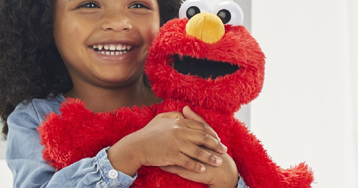 smiling girl holding the sesame street tickliest tickle me elmo doll