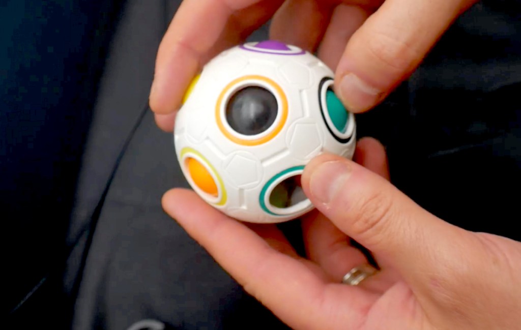 hands holding cube ball with colored balls in holes