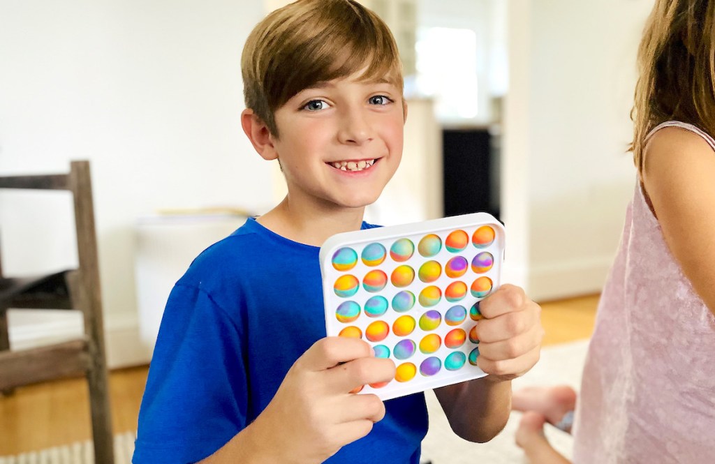 boy holding up white and tie dye pop it fidget toy smiling