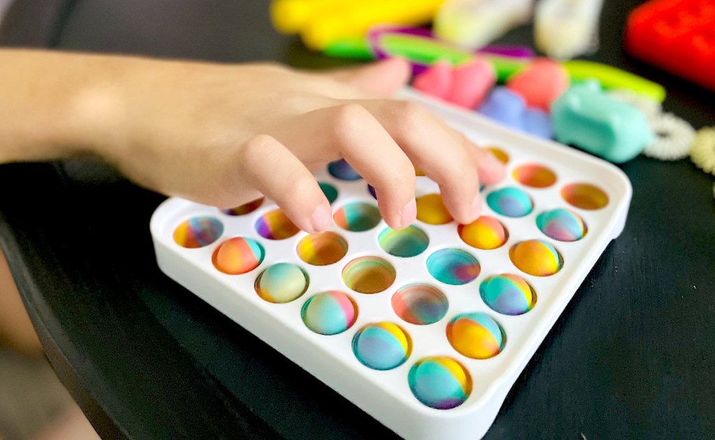 kids hand pushing tie dye bubbles on plastic toy