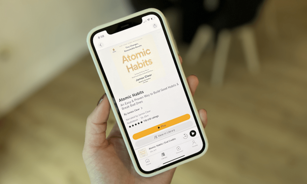 hand holding a phone with atomic habits audible on screen