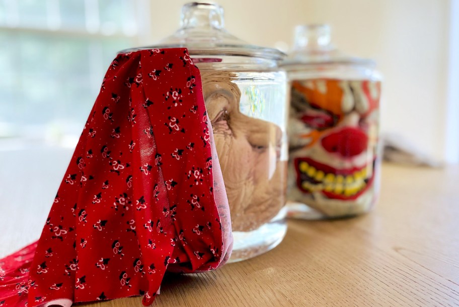 close up of halloween masks in glass jars on wood table