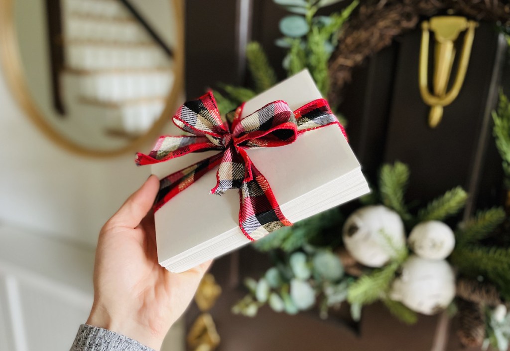 hand holding white envelopes with christmas bow in front of door