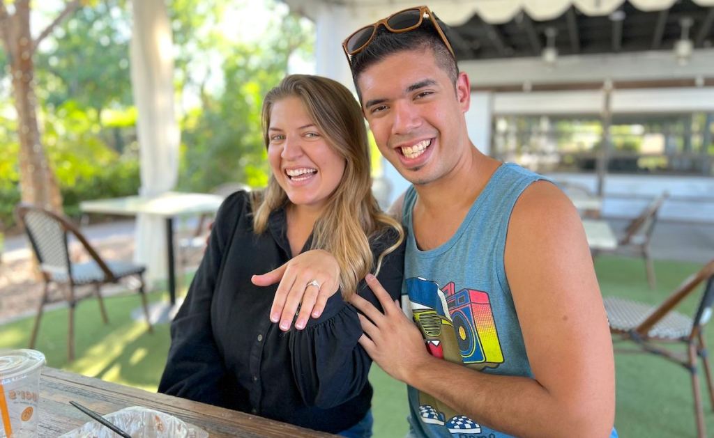 man and woman sitting at table showing off engagement ring