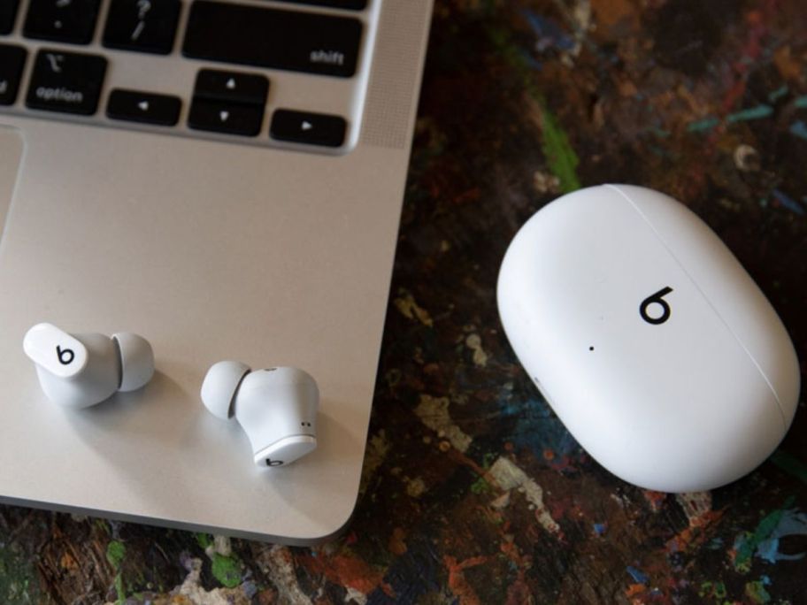 A pair of beats studio buds on a MacBook with their charging case nearby