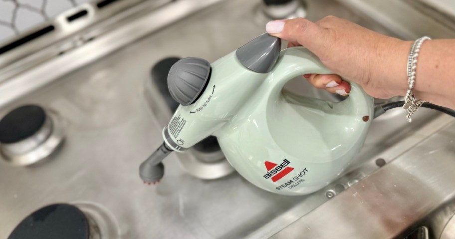 hand using a green Bissell SteamShot to clean a dirty stove