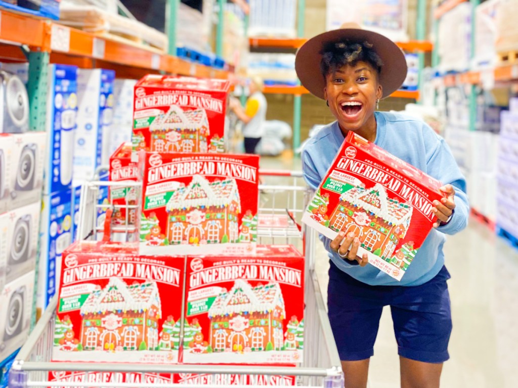 person holding gingerbread mansion boxes inside costco store