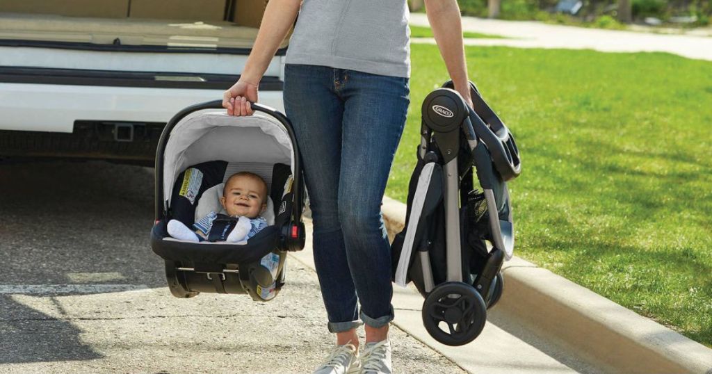 woman holding baby in car seat and folded stroller 