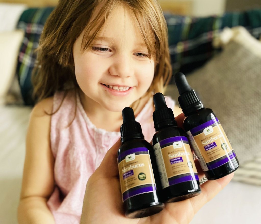 holding 3 bottles of elderberry extract in front of girl