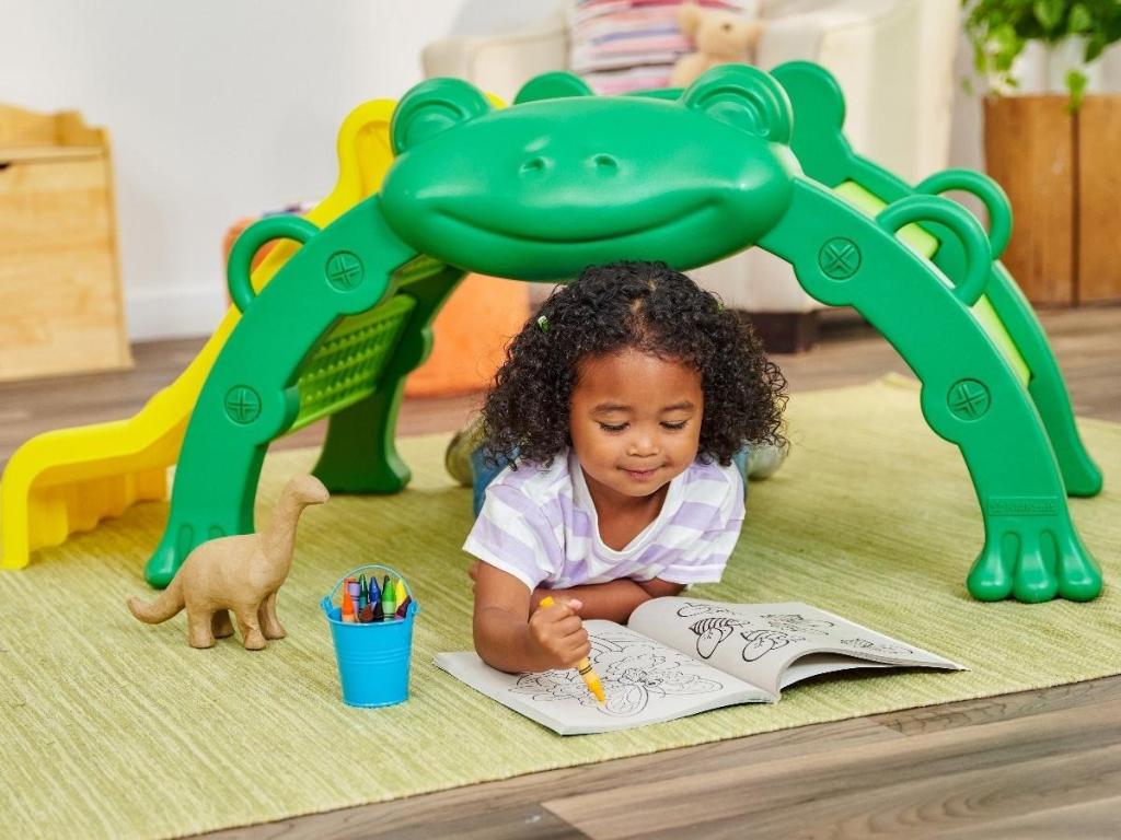 girl sitting under kidkraft frog slide and climber