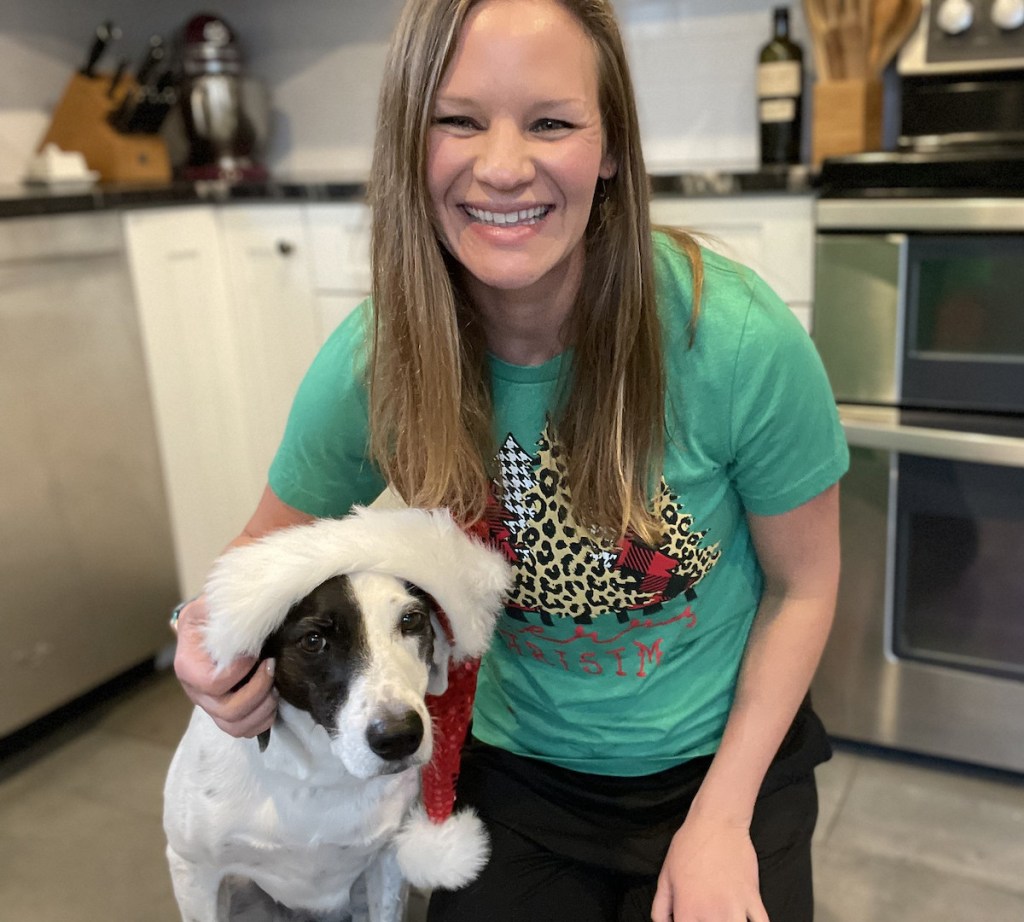 woman kneeling next to dog with santa hat in kitchen