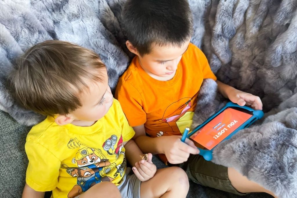 two children sitting on a counch and playing with a Contixo tablet