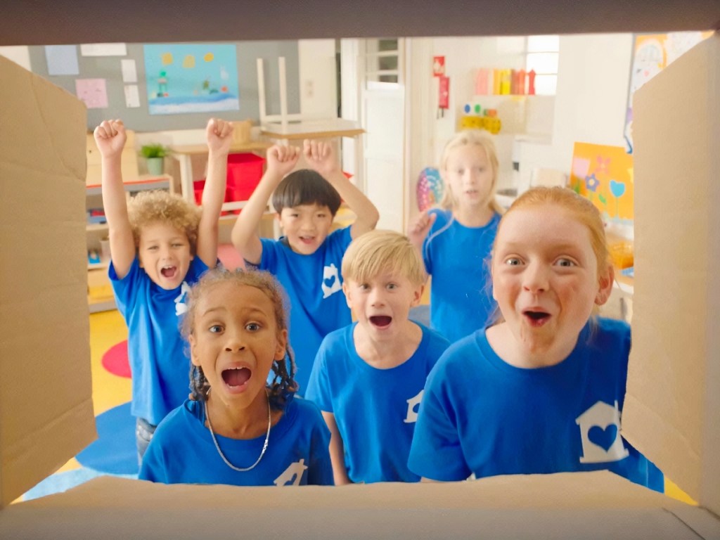 children in blue shirts looking into cardboard box