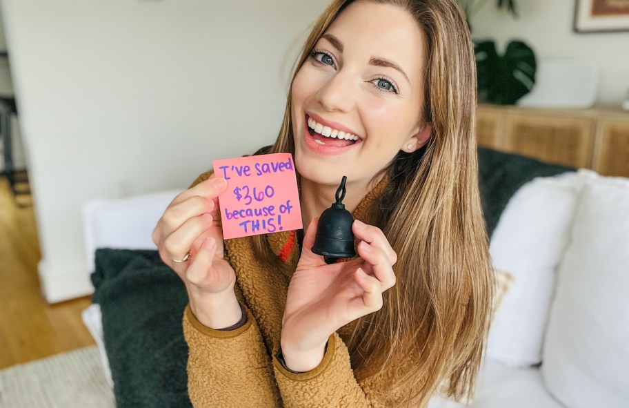 woman holding menstrual cup and pink post it note with savings