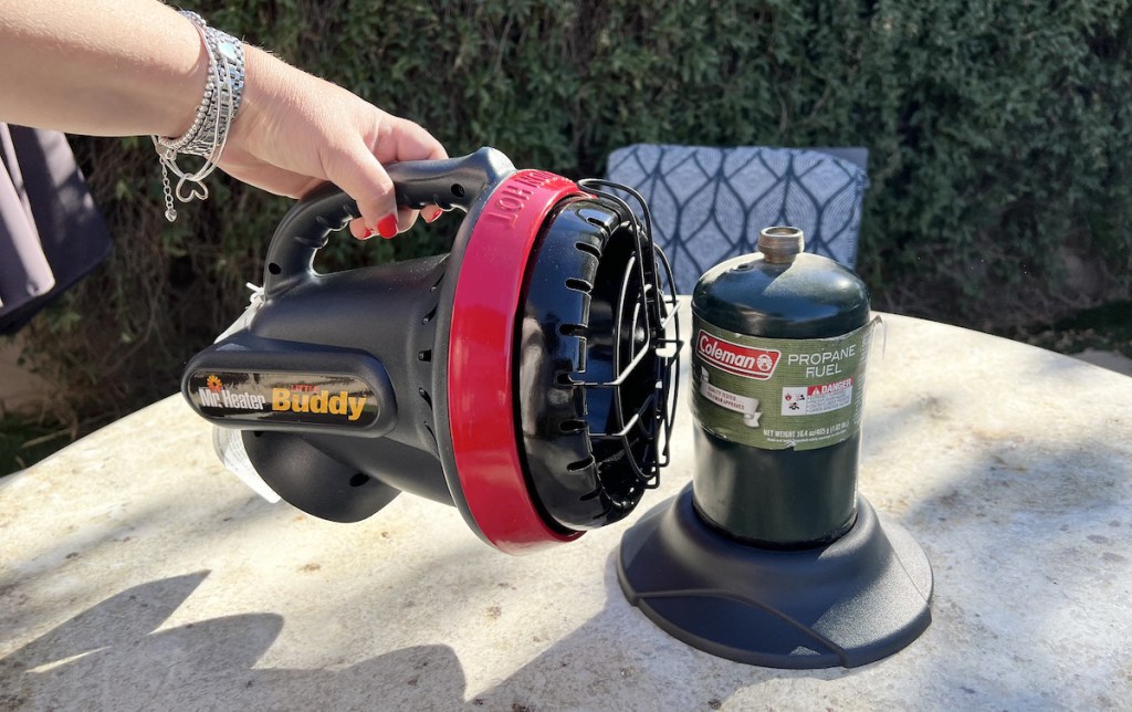 hand holding mini camping heater on outside table with propane tank